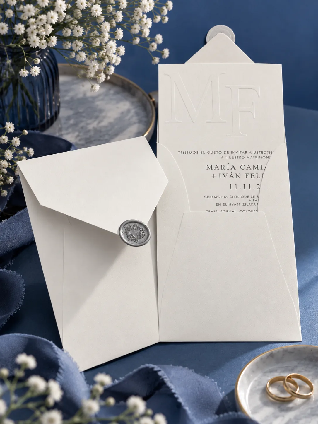 Invitación de matrimonio marfil con monograma en relieve y lacre plateado sobre fondo azul